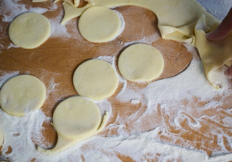 Runde Kreise aus ausgerolltem Erdäpfelteig liegen auf einer bemehlten Arbeitsfläche.