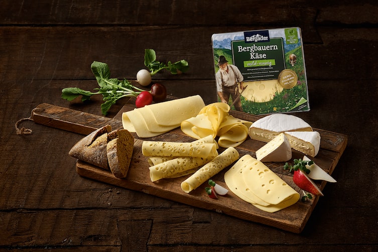 Ein Holztisch voller regionaler Käsesorten von Bergader.