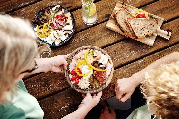 Ein Holztisch voller regionaler Speisen aus der Steiermark auf Holzbrettern, serviert von einer Kellnerin.