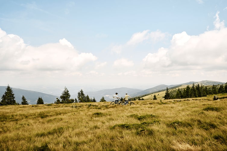 Die zwei Mountainbiker schieben ihr Mountainbike auf einem Panoramaweg im Sommer in der Oststeiermark.