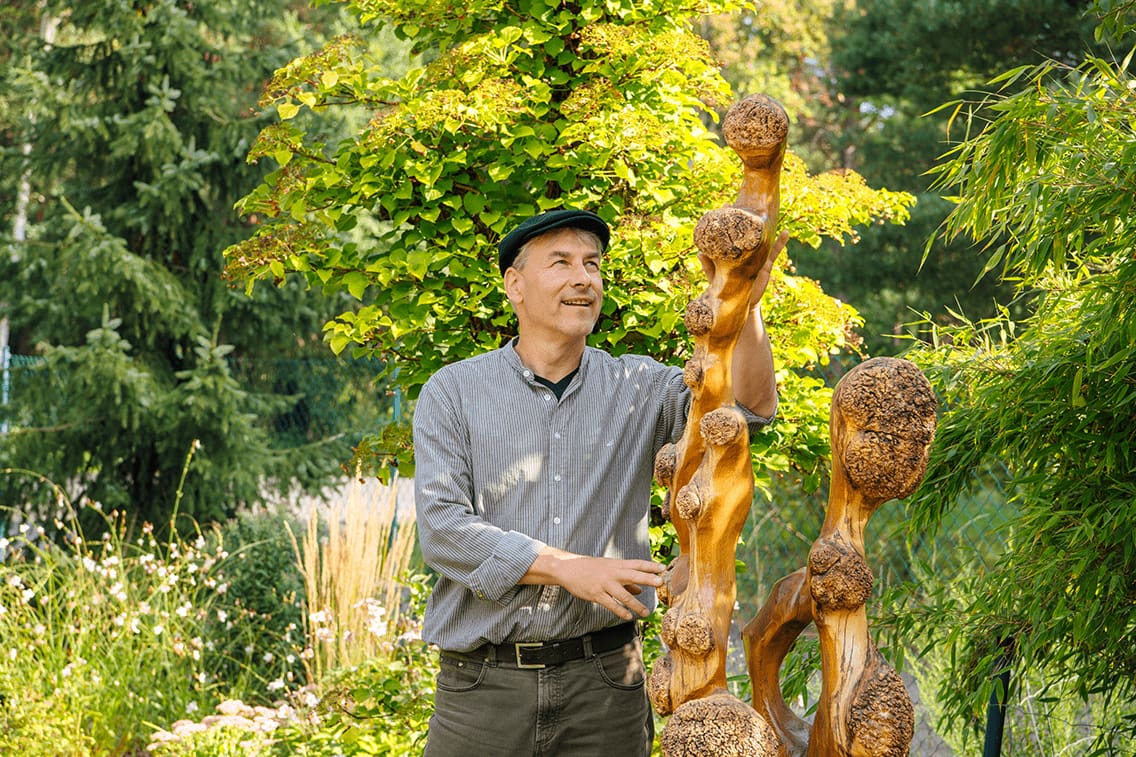 Der Holzkünstler Thomas Schwarz steht neben seinen Statuen im Garten.