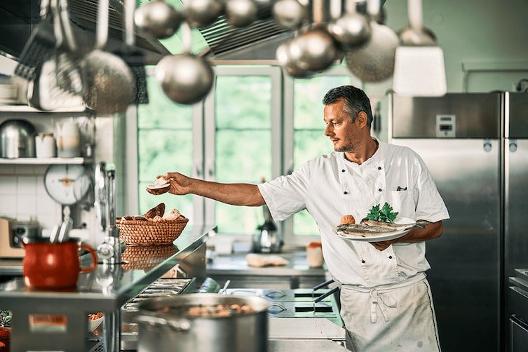 Ein Koch in seiner Küche mit einem Teller frischer Fische in der Hand.