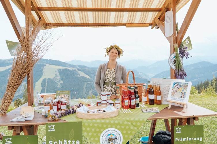 Eine Frau steht vor ihrem Stand am Hochkönig und bietet ihr Produkte an.