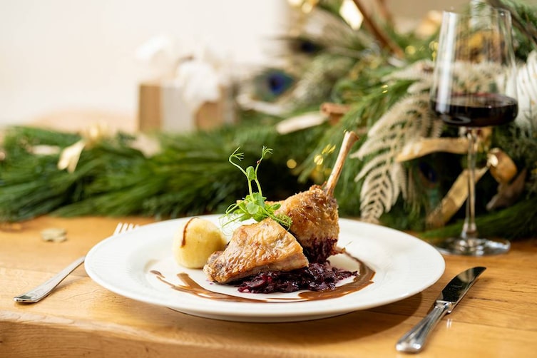 gansl keule mit rotkraut und knödel auf einem teller im weihnachtlichen ambiente
