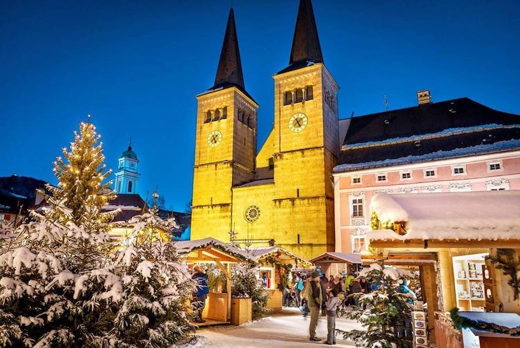 Adventsmarkt in Berchtesgaden mit geschmücktem Christbaum und beleuchteter Stiftskirche bei Abendstimmung.