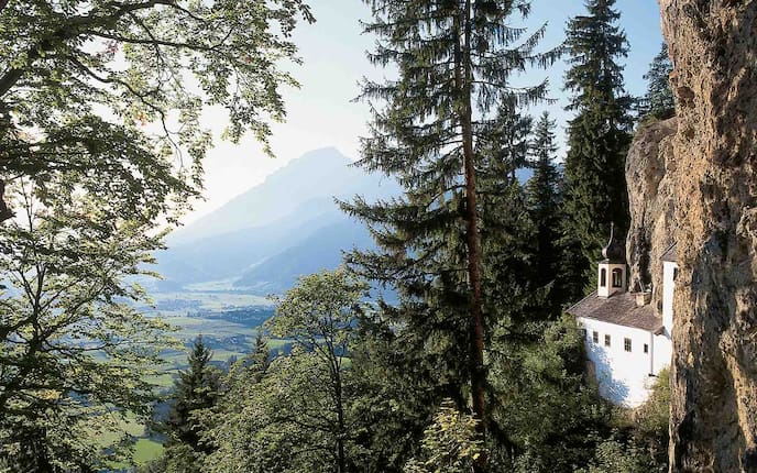 Einsiedelei in den Fels gebaut mit Bäumen und Tal im Hintergrund