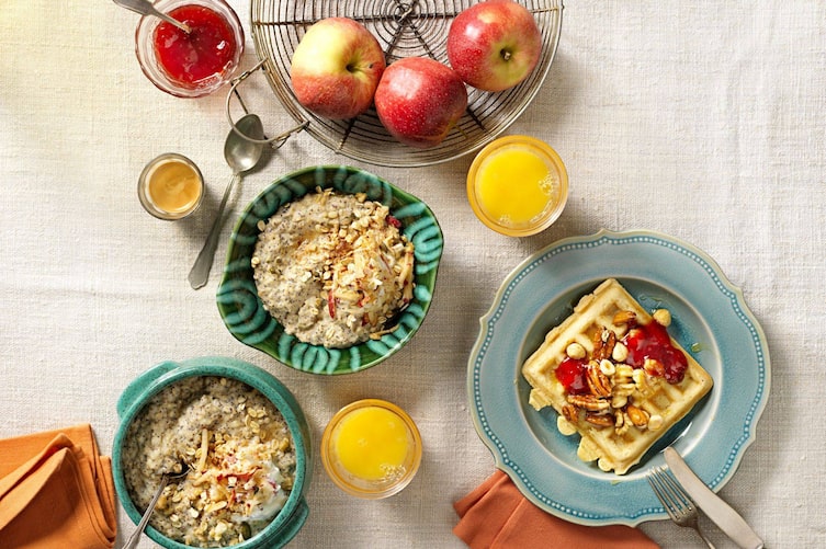 Haferbrei in Schüsserln, Waffeln mit Nüssen, Orangsaftgläser, Espresso, Marmelade, Metallobstkorb mit Äpfeln