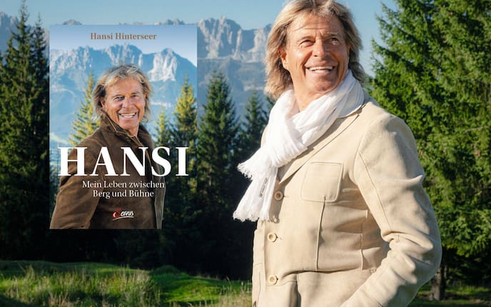 Lachender Hansi Hinterseer steht vor einem Wald und blickt in die Ferne, daneben ist das Cover seines neuen Buches zu sehen.