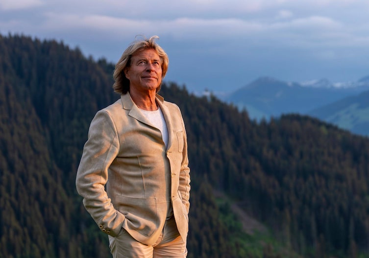 Hans Hinterseer Portrait im Sonnenuntergang, im Hintergrund sind Berge und Wälder zu sehen.