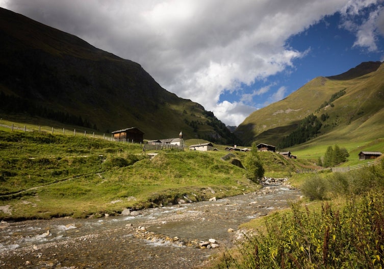 Fanealm im Sommer mit Bach, grünen Wiesen, Bergen und wolkigen Himmel