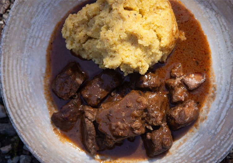 Tiefer grauer Keramikteller mit Polenta und Rindergulasch. Nahaufnahme von oben fotografiert.