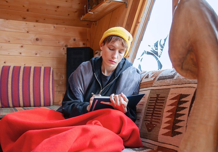Sigrid Horn sitzt auf einem Sofa zugedeckt und schreibt in ein Buch