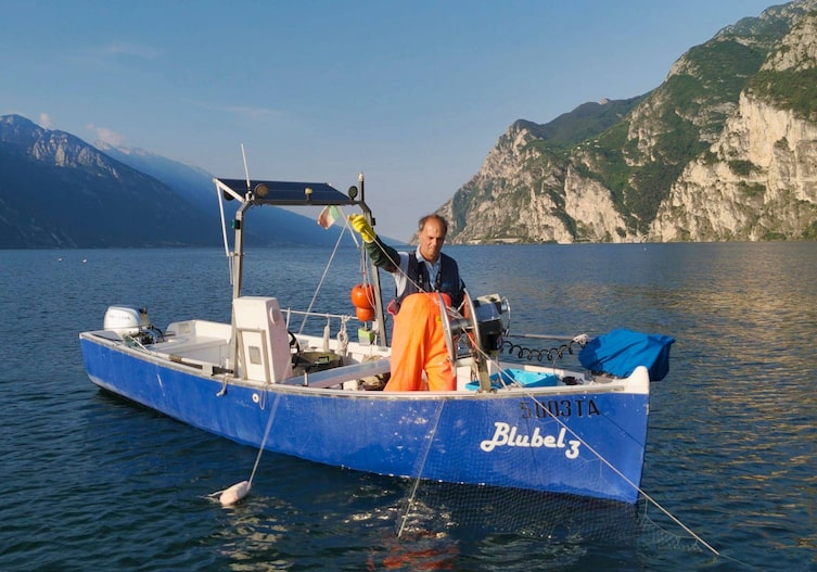 Ein Fischer holt ein Netz auf einem kleinen Fischerboot auf dem Gardasee ein. Es ist Sommer.
