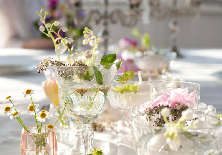 Maiglöckchen, Margariten und andere Wiesenblumen sind lose in alte unterschiedliche Gläser aller Sorten gestellt und werden am Tisch als Vase benutzt