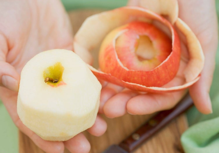 Geschälter Apfel, die Apfelschale liegt daneben, beides wird in der Hand gehalten