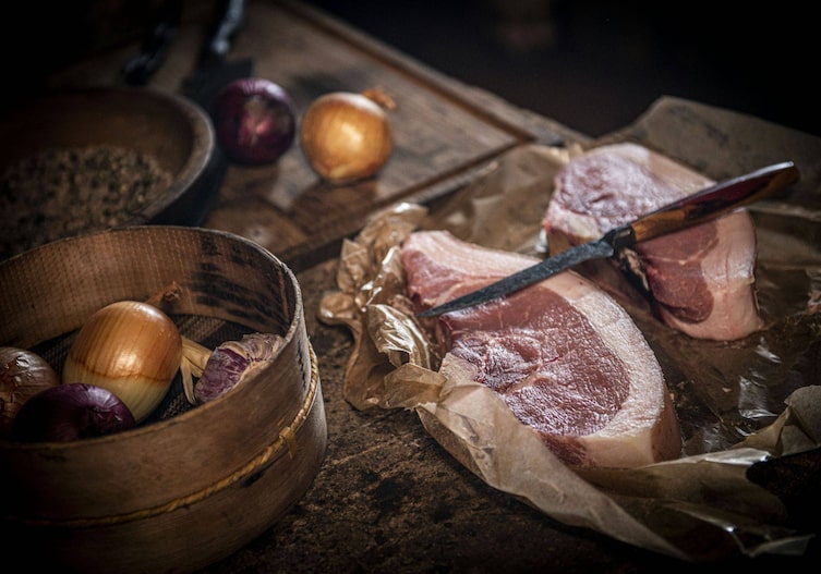 Zwei rohe scheiben Fleisch mit Fettrand, Messer, Zwiebel, altes Mehlsieb
