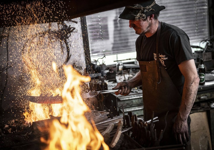 Ein Schmied hält ein Sägeblatt ins offene Feuer