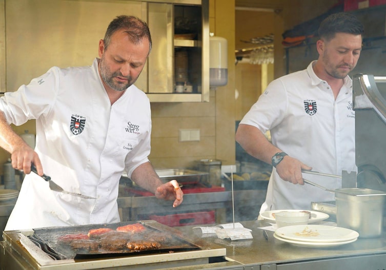 Fritz und Tamino Grampelhuber stehen in einer Großküche und bereiten Burgerfleisch am Griller zu.