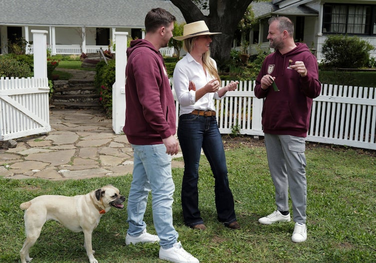 Fritz, Tamino Grampelhuber und Elizabeth Poett stehen im Garten in der Wiese vor einem weißen Zaun und sprechen miteinander. Im Hintergrund ist ein großes weißes Haus mit Veranda zu sehen.
