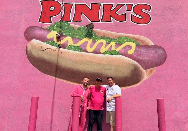 Fritz und Tamino Grampelhuber und Richard Pink stehen vor einer riesigen pinken Wand mit einem riesigen Hot Dog, darüber steht: Pink's