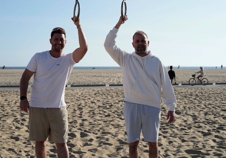 Fritz und Tamino Grampelhuber posieren für ein Foto an einem Strand, im Hintergrund ist das Meer zu sehen