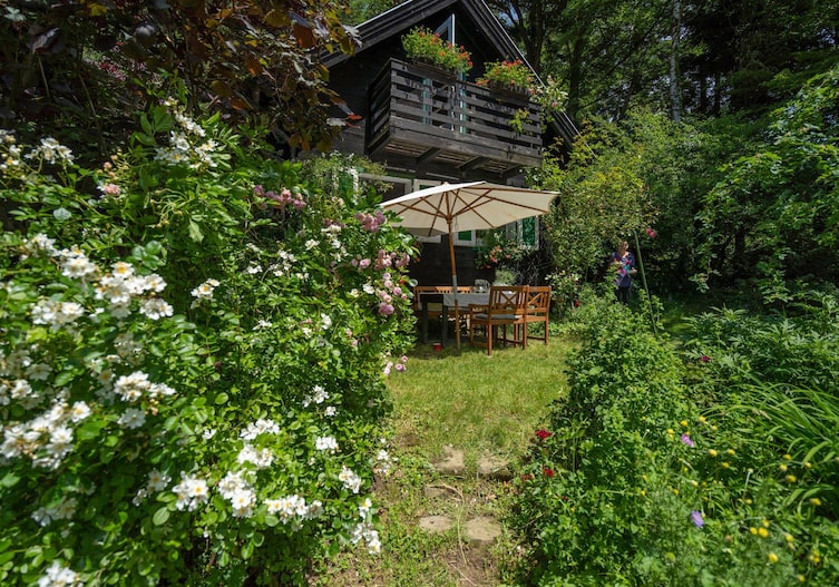 Rosengarten mit Blick auf das Gartenhaus mit Gartentisch und Sonnenschirm