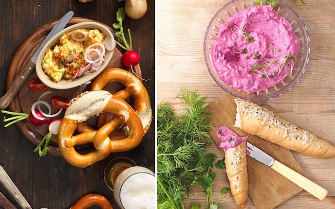 Obazda mit Laugenbrezen, Bier, Radieschen auf einem Holzbrett. Roter Rüben Aufstrich in einer kleinen Glasschüssel, daneben liegt ein Bund Dille, ein Jausenbrett mit Salzstangerl und Buttermesser.