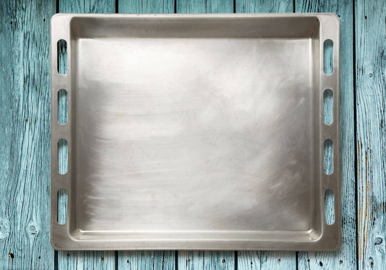 unbeschichtetes sauberes Backblech mit leichten Putzkratzern auf einer hellbauen Holzoberfläche abgestellt