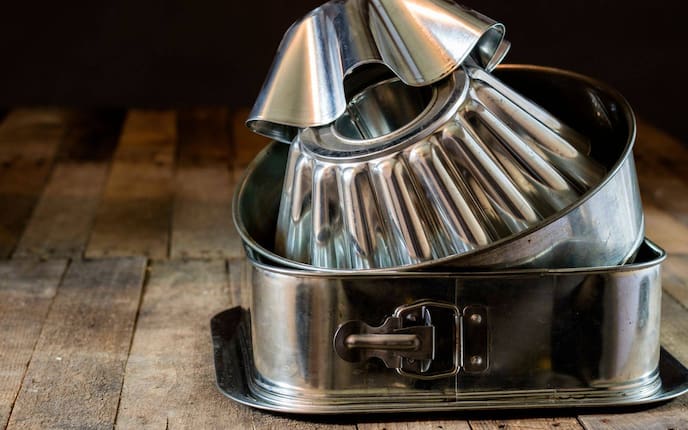 Gewellte Kuchenformen, Tortenspringform rund und eckig, Serviertablett, alles aus Blech, steht auf einem Holzuntergrund und ist übereinander gestapelt.