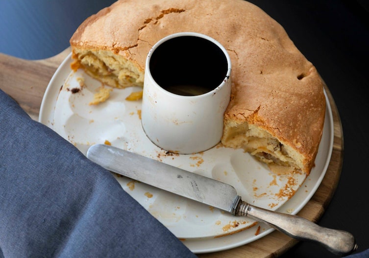 Apfelkuchen noch in der Springform aufgeschnitten, die Hälfte fehlt schon, daneben liegt ein altes Buttermesser.