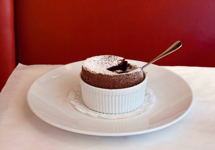 Schokosoufflé auf einem weißen Teller, darin steckt ein Dessertlöfferl