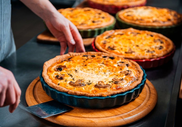 Pikante Tarte fertig gebacken auf einem Holzteller, noch in der Backform