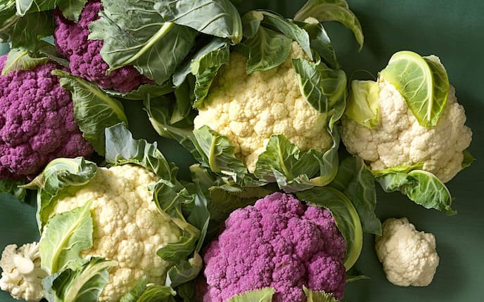 weiße und rote frische Karfiolköpfe mit Blättern auf einer grünen Unterlage