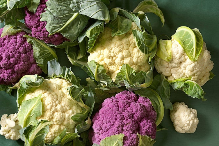 weiße und rote frische Karfiolköpfe mit Blättern auf einer grünen Unterlage