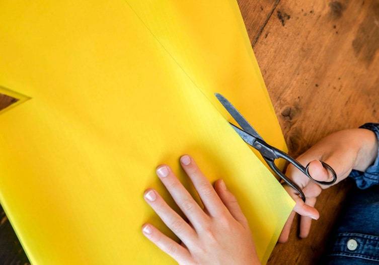 Kinderhände schneiden mit einer Schere den Stoff für den Drachen zurecht.