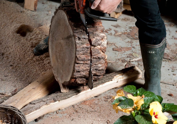 Ein Mann der eine dickere Holzscheibe in der Mitte auseinanderschneidet.