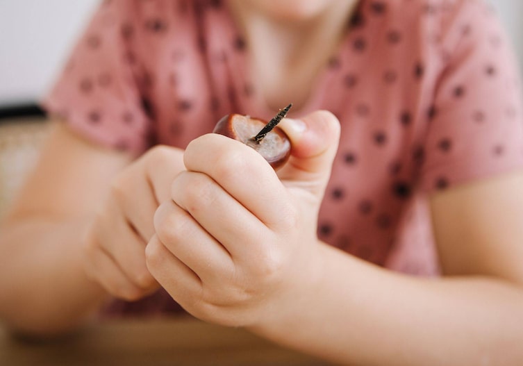 Kinderhände, die mit einem Kastanienbohrer durch eine Kastanie bohren.