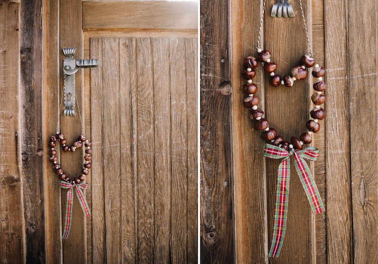Alte Holztür mit einem verschnörkeltem Türgriff, daran hängt an einer Schnur ein Kastanienherz mit einer karierten Schleife.