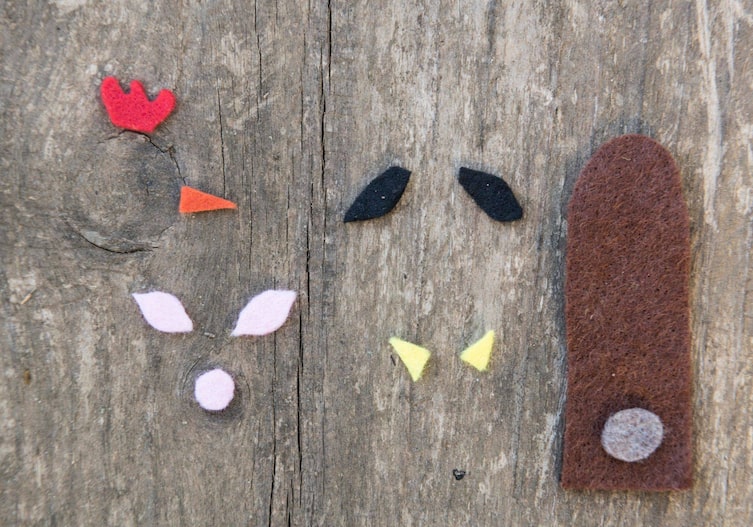 bunte Filzteilchen für Schnabel, Ohren, Nase auf einer Holzunterlage aufgelegt.