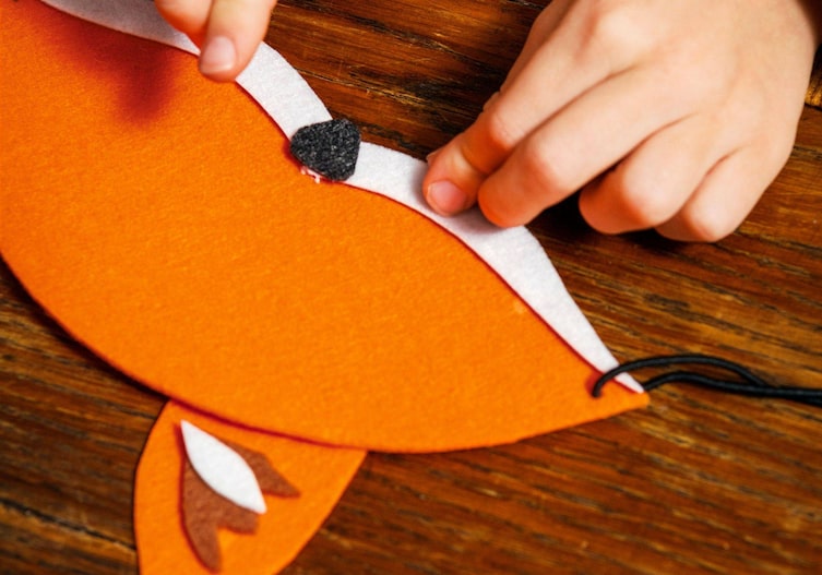 Kinderhände kleben das Zubehör auf die Fuchsmaske (Fuchsbart, Nase)