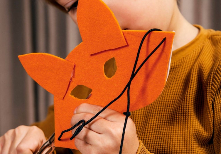 Kinderhände schneiden zwei Augenlöcher in die Fuchsmaske