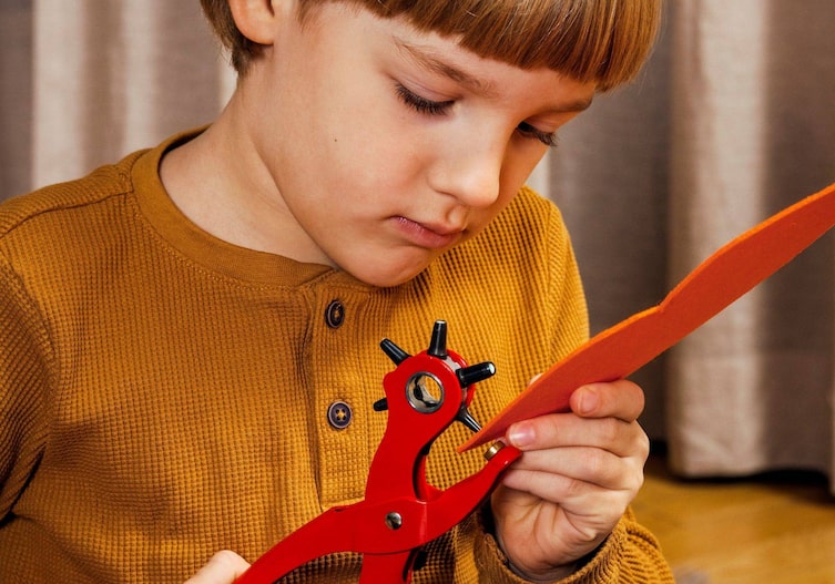 Ein Kind stanzt mit einer Lochstanze ein Loch in den Filz, für das Gummiband.