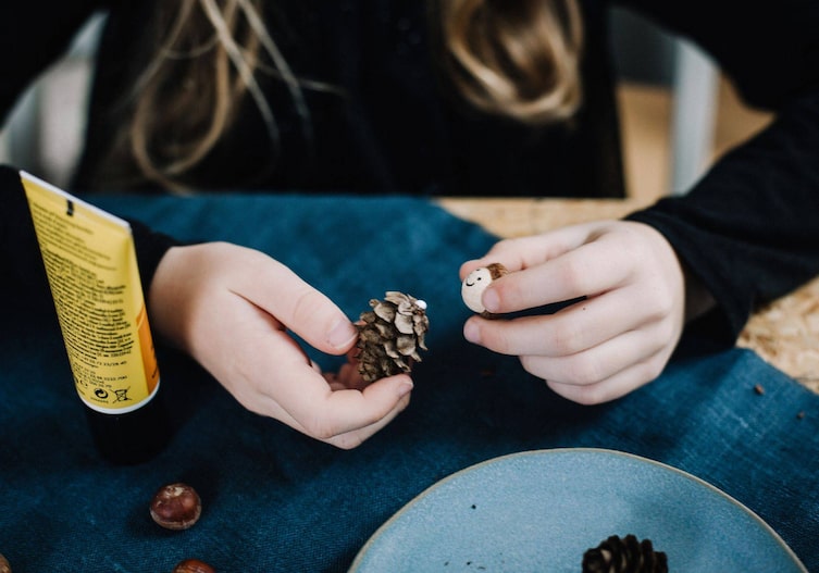 Bockerl, Holzkugel mit Gesicht und Eichelhut werden von Kinderhänden zusammengeklebt.