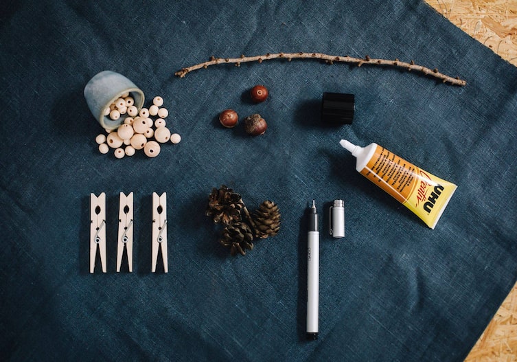 Holzkugeln, Holzkluppen, Bockerl, Eicheln, Uhu, Fineliner auf einem dunkelblauen Stoff ausgebreitet und von oben fotografiert.