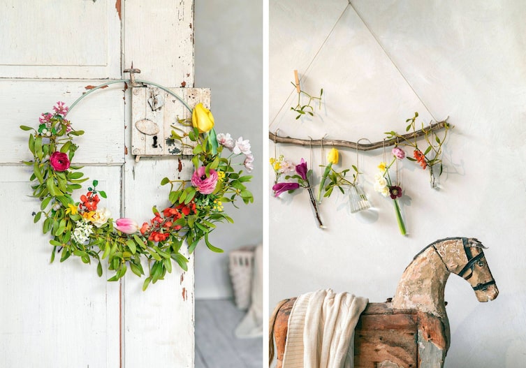 Alte weiße Tür mit Blumenkranz der zur Hälfte mit Misteln und Tuplen und Ranunkeln geschmückt ist. Daneben ist ein Holzpfert mit hängenden Bumenvasen mit frischen Ranunkeln, Misteln, Tulpen, die auf einen Ast gebunden sind, der an der Wand hängt.