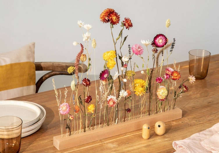 Ein Holztisch, auf dem eine Holzleiste steht und mit Trockenblumen geschmückt ist.