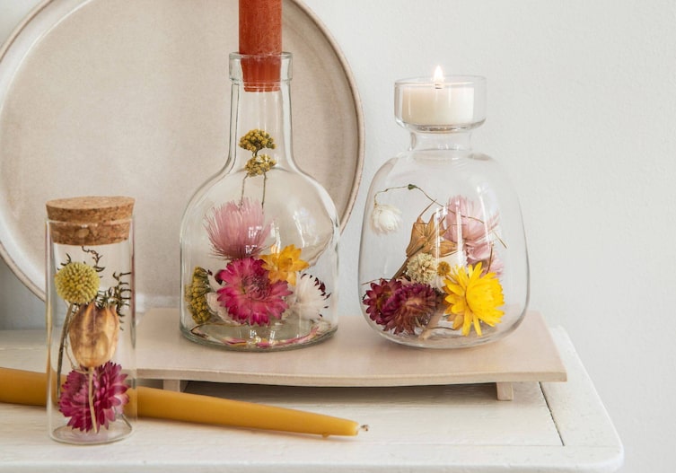 In Glasflaschen, die zu Kerzenständern umfunktioniert wurden stecken bunte Trockenblumen.