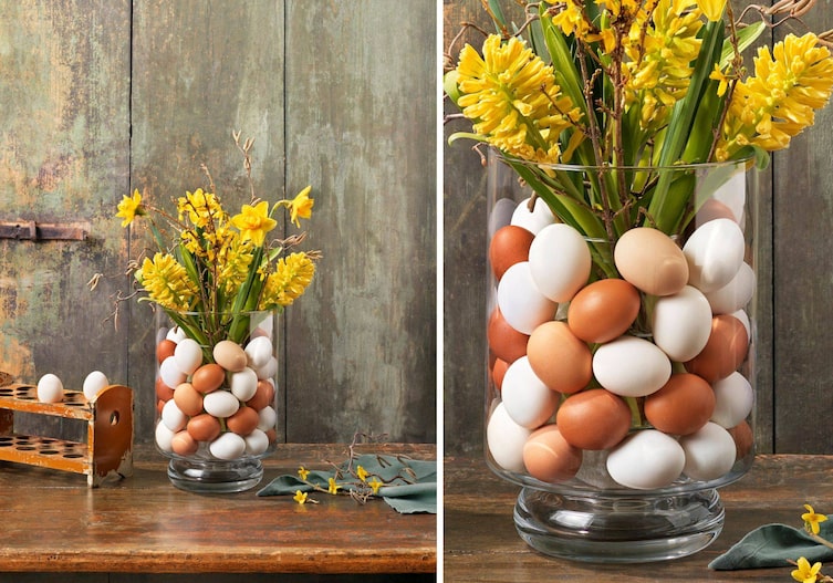 Eine große Glasvase, die mit braunen und weißen hart gekochten Eiern gefüllt ist. Darin steckt eine weitere Glasvase, in der ein gelber Blumenstraus steht.