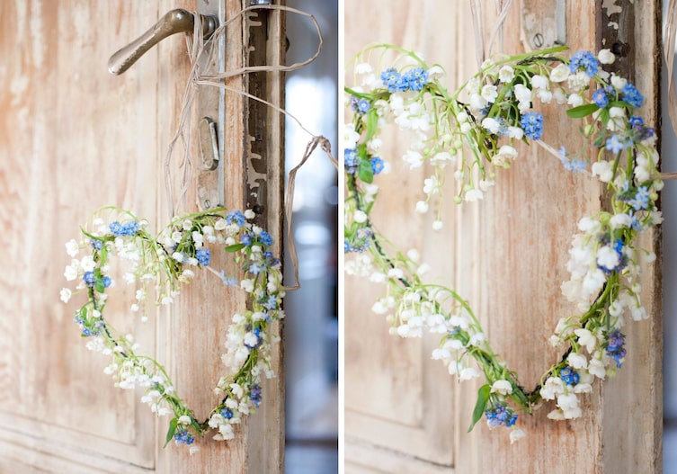 Eine alte Holztür, an deren Griff ein Blumenherz hängt, das aus einem dünnen Draht gebogen ist und drumherum Maiglöckchen und Vergissmennicht gebunden sind.