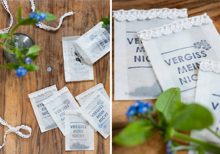 Kleine Papiersackerl auf denen Vergiss mein nicht steht - darin sind Samen vom Vergissmeinnicht. 7 Sackerl liegen auf dem Tisch, eines ist offen und die Samen liegen auf dem dunklem Holz, daneben steht eine kleine Blumenvase mit Vergissmeinnicht und die Blumen liegen auch am Tisch. Die Sackerl sind mit einem gehäkeltem Band verziert, das Bind liegt auch am Tisch